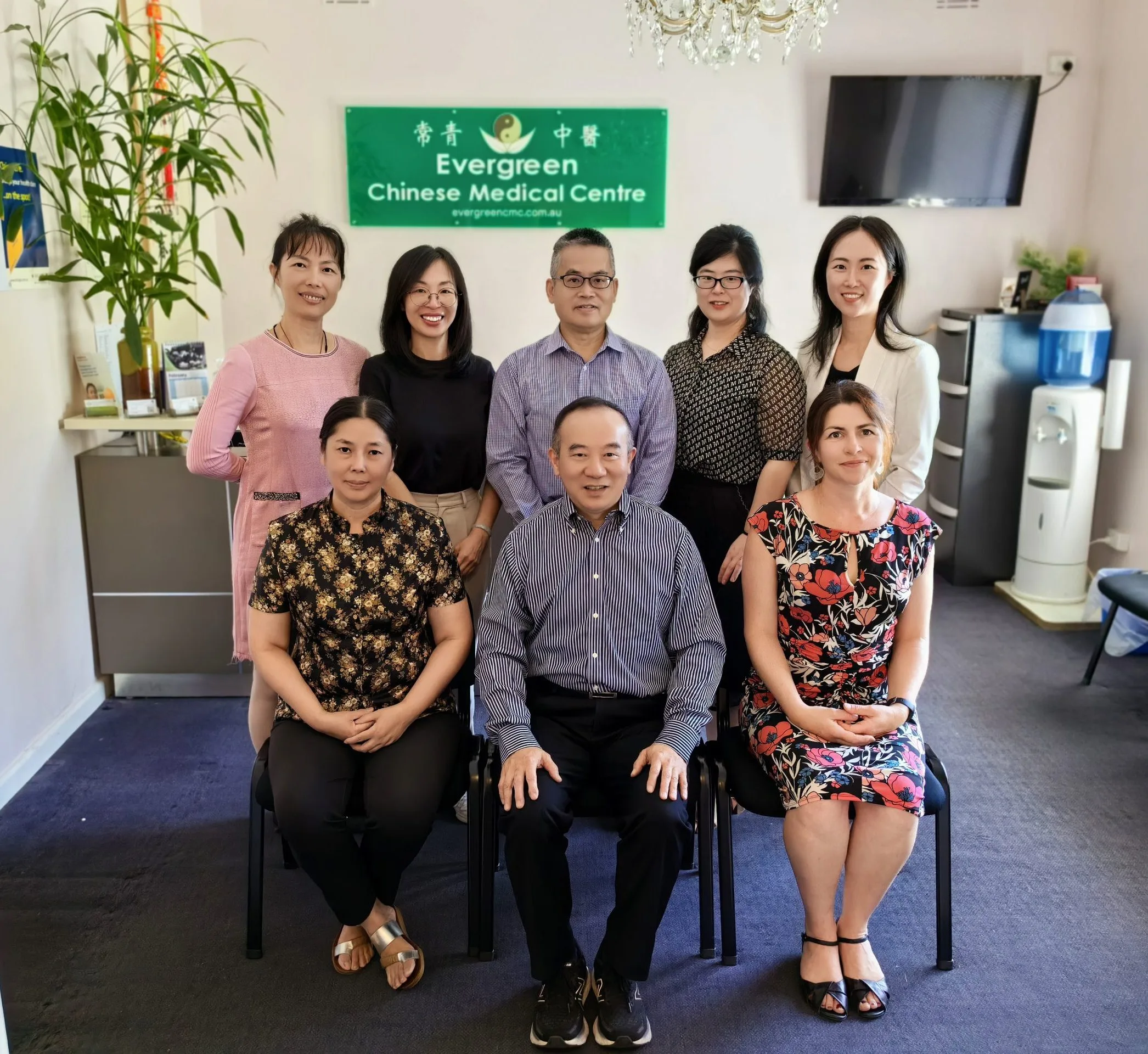The Evergreen Chinese Medical Centre team gathered indoors beneath the clinic's green sign